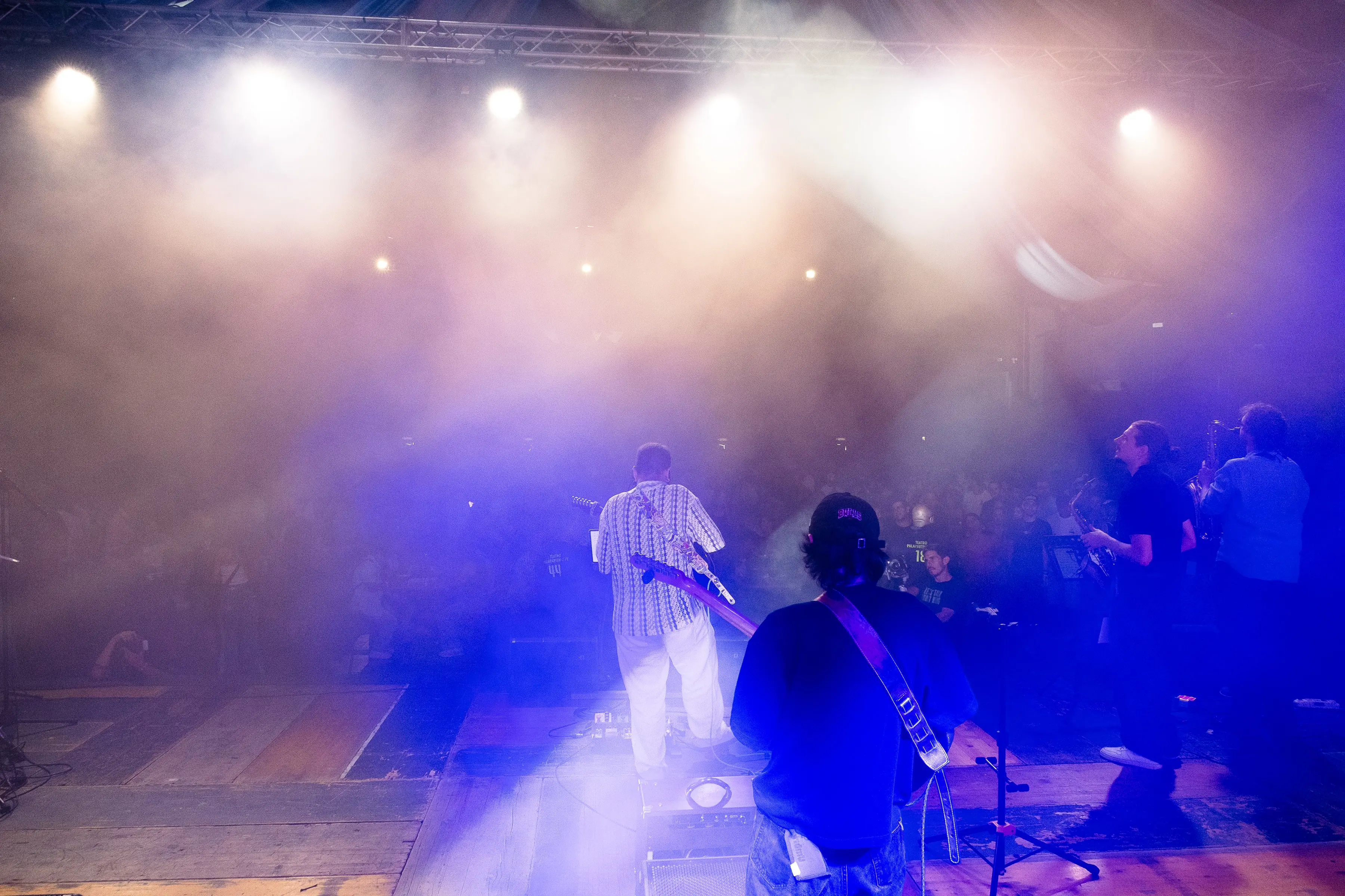 Full band performing on stage as the crowd cheers under blue and purple lighting
