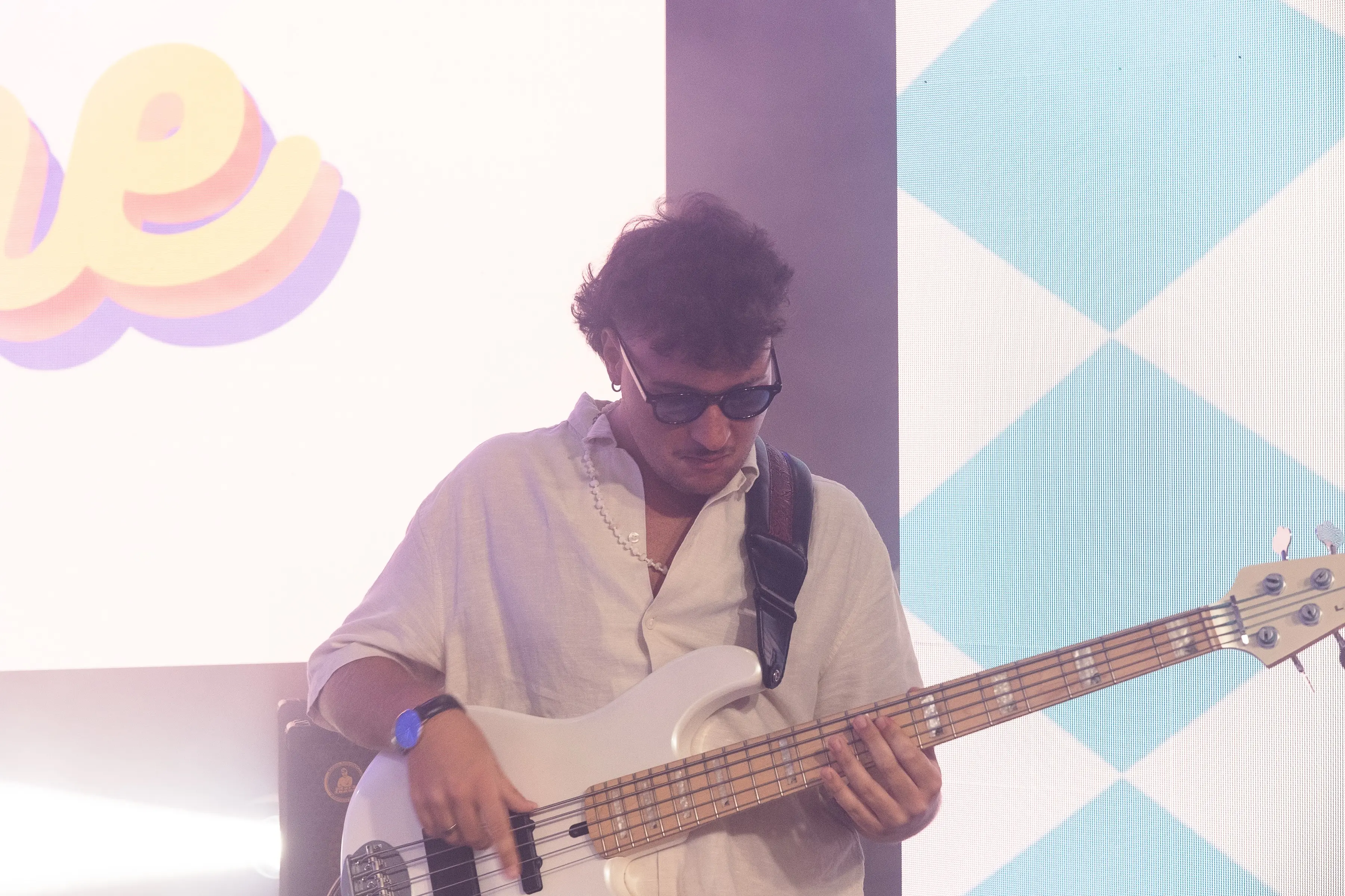 Bassist in sunglasses playing a white bass under colorful stage light