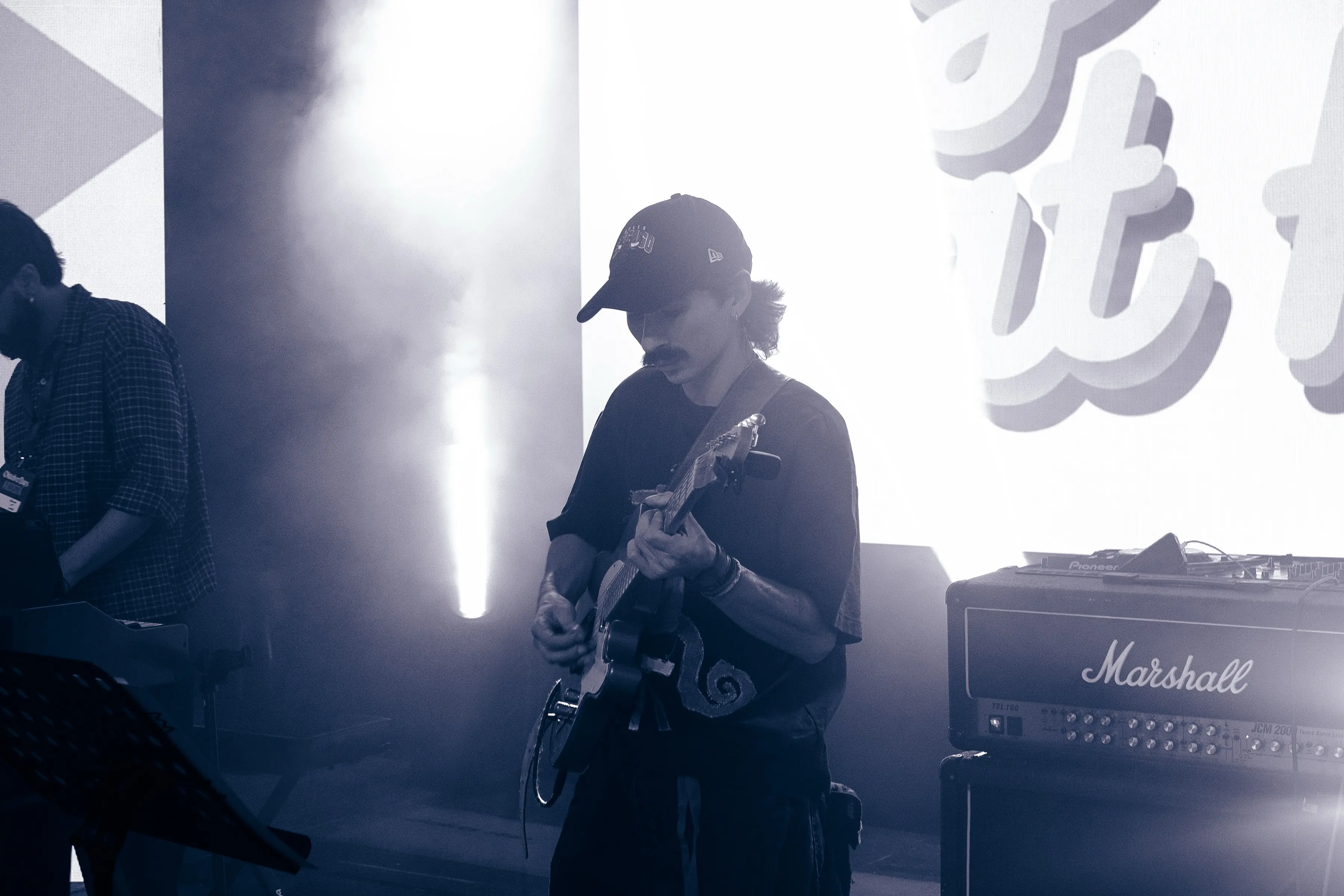 Guitarist playing beside a Marshall amp under cool blue stage light